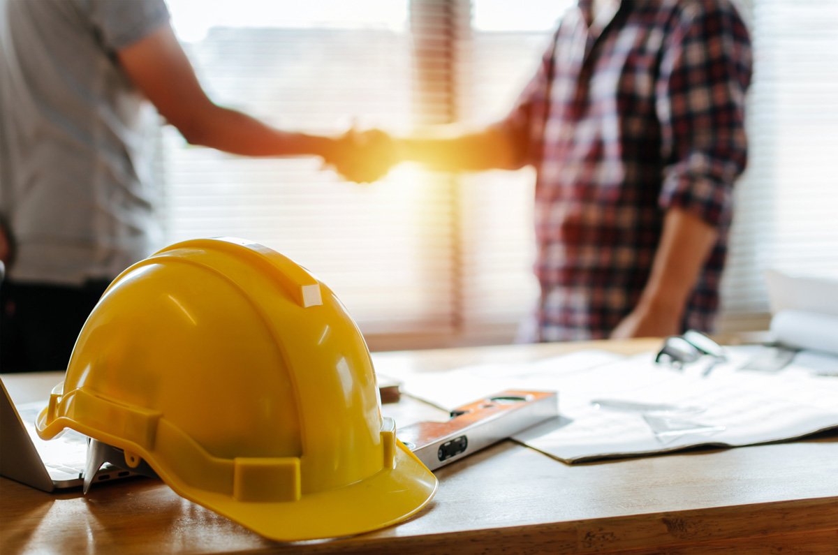 remodeling-contractor-el-paso Two people shaking hands behind a yellow hardhat on a desk in El Paso.